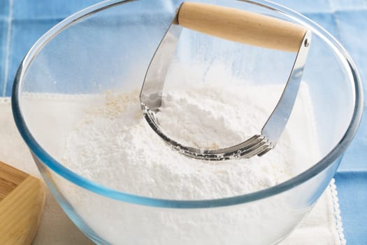 Handheld pastry blender in bowl with flour.