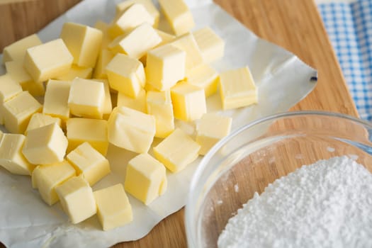 Fresh butter cubes on cutting board with bowl of flour.