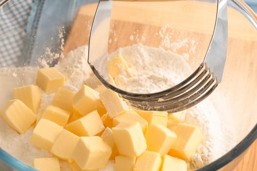 Butter in bowl with flour and handheld pastry blender.