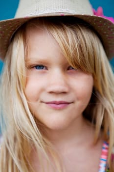 Closeup of face of cute smiling young girl with stylish hat outside against blue wall background