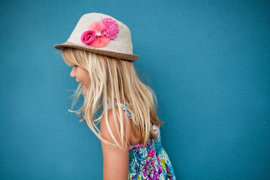 Side view of cute young girl wearing stylish hat against blue wall background