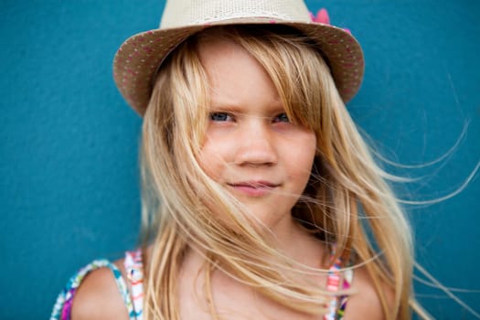 Closeup portrait of cute young girl with stylish hat outside against blue wall background