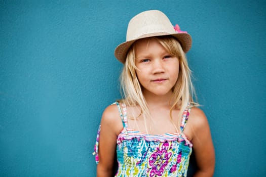 Portrait of cute young girl in relaxed pose wearing stylish hat outside against blue wall background