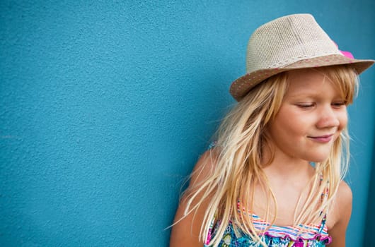 Cute young girl wearing stylish hat smiling outside against blue wall background