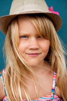 Closeup portrait of cute young girl with stylish hat outside against blue wall background