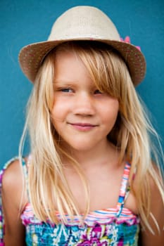 Portrait of cute smiling young girl wearing stylish hat outside against blue wall background and looking to side