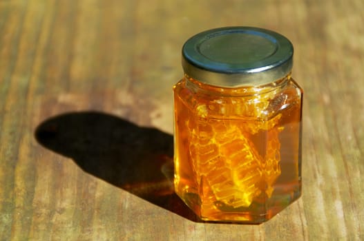 A jar of pure amber colored local honey glistens in the sun, inside the jar is also a piece of the honeycomb it came from.