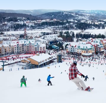 Mont-Tremblant, Canada - February 9, 2014: Skiers and snowboarders are sliding down the main slope at Mont-Tremblant. Mont-Tremblant Ski Resort is acknowledged by most industry experts as being the best ski resort in Eastern North America.