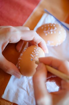 traditional decorating of the easter eggs by the woman,visible woman's hands,visible in the background another easter egg,shallow dof.