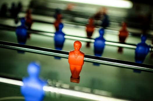 A table football in the pub, visible  figure of a toy mini football player in the red colour and blur other figures of football players (red and blue).
