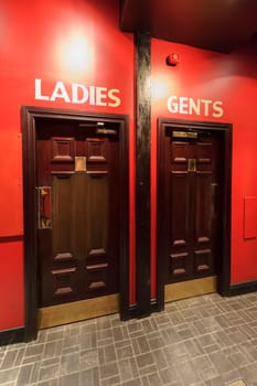 Entrance to the WC,  toilets in the restaurant, separate for ladies,women and gents,menon the red wall, dark brown door.