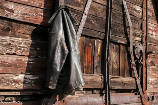 Vintage leather male jacket hanging on the wall of old wooden railway wagon as background