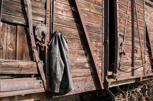 Vintage leather male jacket hanging on the wall of old wooden railway wagon as background