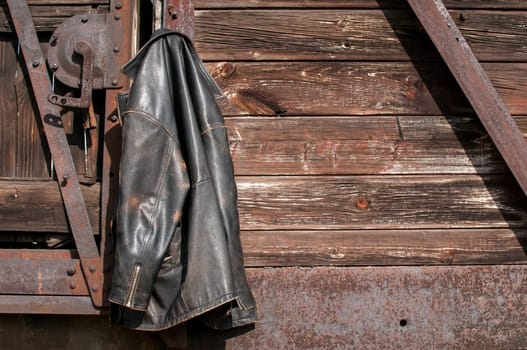 Vintage leather male jacket hanging on the wall of old wooden railway wagon as background