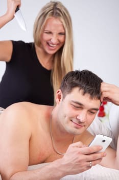 Man is cheating on phone, angry woman with knife behind him