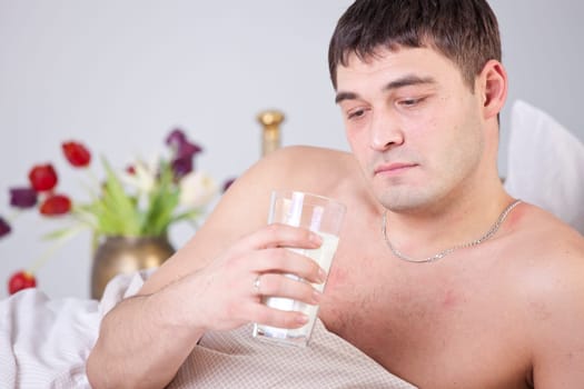 Sick and unhappy man with glass milk on bed