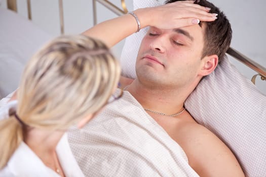 Sick man in bed, female doctor puts her hand on forehead