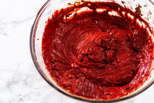 Mixing wet ingredients in a large glass mixing bowl to bake red velvet cupcakes with white chocolate ganache frosting.