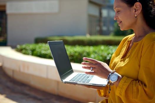 Close-up portrait of a charming multi ethnic woman talking with business partners via video link, using a laptop with black blank mockup digital screen with free advertising space for promotional text