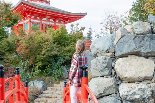 Woman in red plaid shirt enjoying nature walking in Japanese Garden with red pagoda