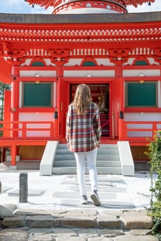 back view of unrecognizable Woman in red plaid shirt enjoying nature walking in Japanese Garden with red pagoda