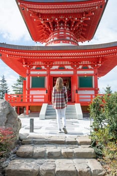 back view of unrecognizable Woman in red plaid shirt enjoying nature walking in Japanese Garden with red pagoda