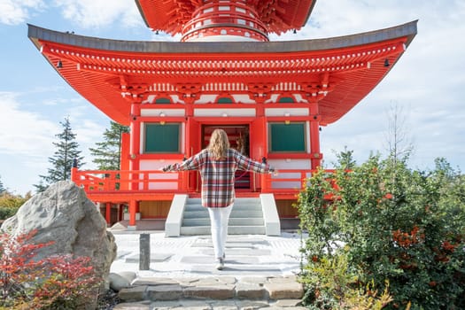 back view of unrecognizable Woman in red plaid shirt enjoying nature walking in Japanese Garden with red pagoda