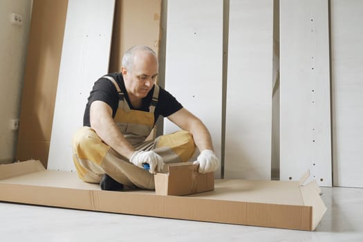 A male worker unpacks a box of cabinet furniture parts. Overall plan.