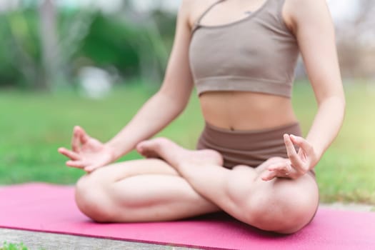 Asian woman in sporty outfit relaxing meditating feeling zen like on fitness mat in public park outdoor. Healthy active lifestyle.