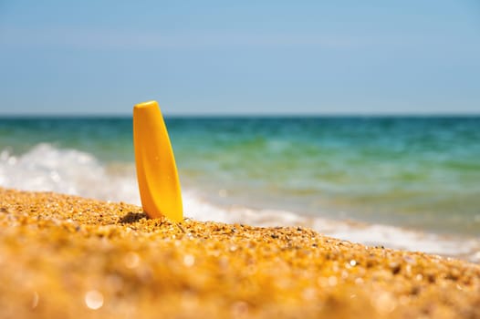 Sunscreen in the sand against the background of the sea. Yellow tube of sun skin care product without label. Mockup for your brand.