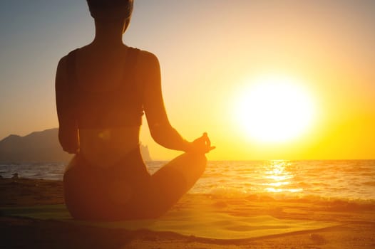 girl does yoga and meditates in lotus position on the beach. silhouette of a young woman by the sea at dawn, healthy lifestyle concept, view from the back.