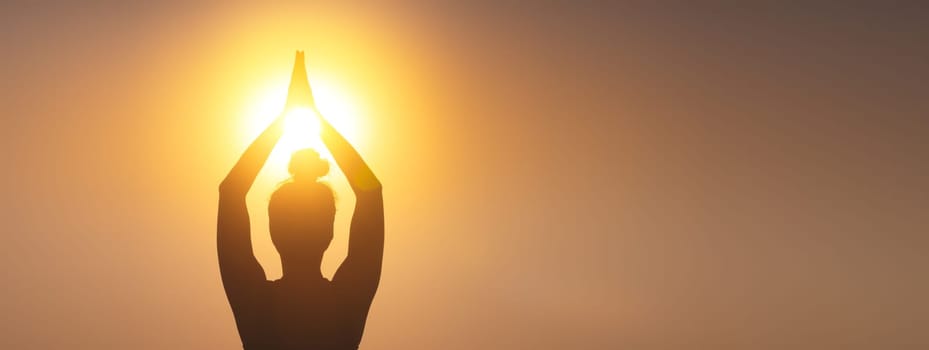 silhouette of a woman raising her hands, praying for God's blessings in the light of sunset or sunrise, practicing yoga and meditation in nature, concept of religion, freedom and spirituality.