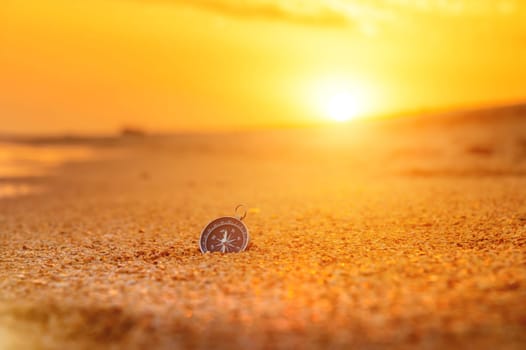 compass on the beach with sunrise or during sunset, orange sky with bright sun rays, travel concept. no people