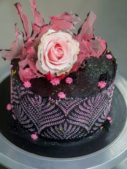 frosted icing black decorate cake for birthday celebration, real rose topping and pink sweet swirls in professional kitchen