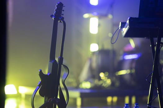 A guitar stands alone on a stage, subtly lit, waiting for the performance.