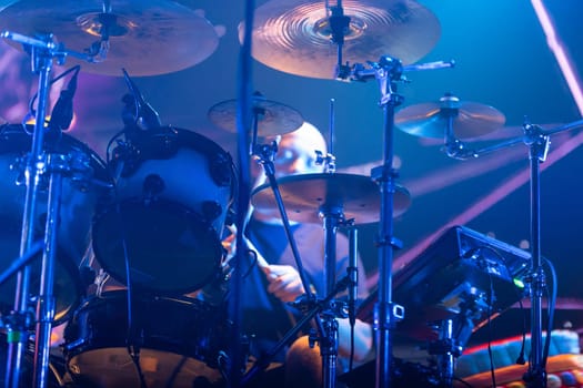 A drum set on a stage, dramatically illuminated by bright, colorful lights.