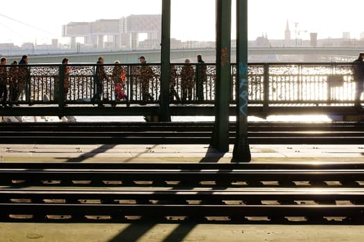 Cologne,Germany – February 02,2014: Walkers cross the Hohenzollern Bridge over the Rhine River with a view of the Rheinauhafen  and enjoy the sun on February 2nd,2014 in Cologne.