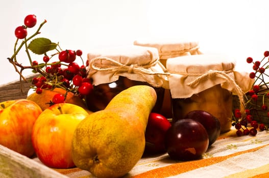Preserved fruit in jars and fresh on wooden tray