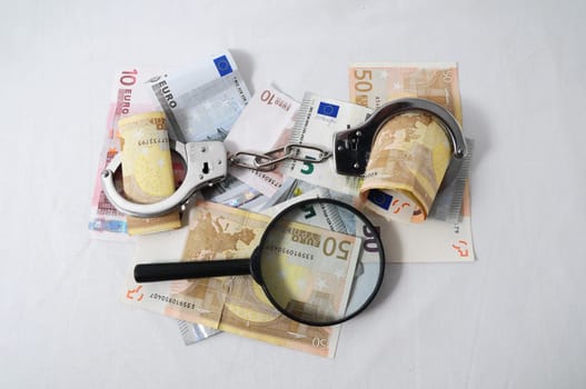 Financial Concept Loupe, Handcuffs and Money on a White Background