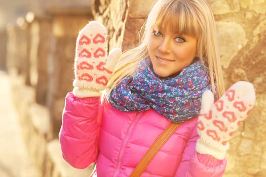 Beautiful blonde girl in a pink jacket with a blue scarf and mittens