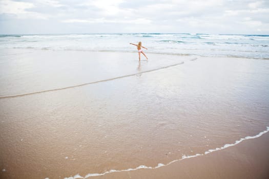 Young girl in swimming suit playing in shallow water at the beach