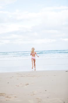 Young girl in swimming suit running towards water at beach