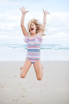Young cute girl in swimming suit having fun at the beach by jumping in air