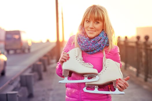 Beautiful smiling blond woman with ice skates on the bridge