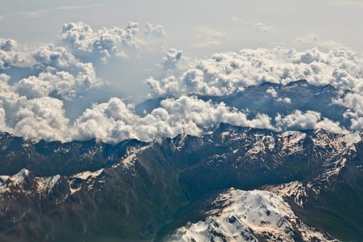 A photograph of several peaks in the Alps covered with snow and with thin clouds above