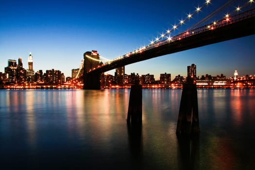 New York City Manhattan skyline panorama with Brooklyn Bridge and office skyscrapers building in at dusk illuminated with lights at night