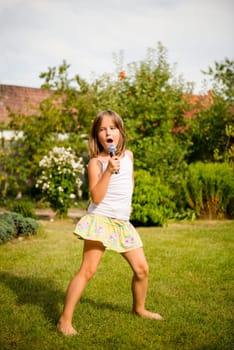 Happy childhood - child singing with microphone outdoor in backyard