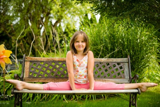 Child (little girl) performing gymnastic pose on bench outdoor in backyard
