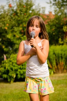 Happy childhood - child singing with microphone outdoor in backyard