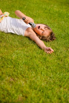 Child singing with microphone and lying on grass - outdoor lifestyle